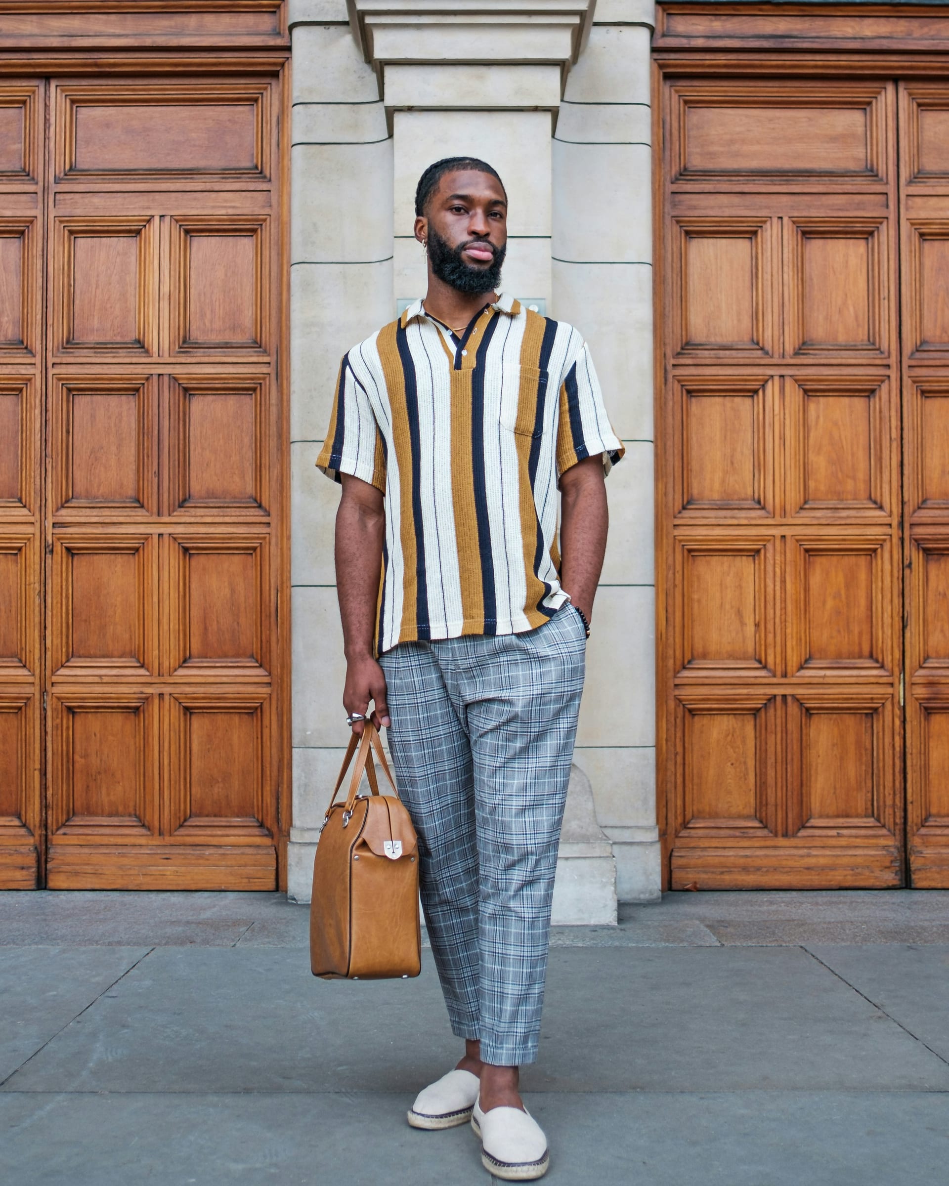 Full-body portrait in a bold striped shirt by ornate wooden doors